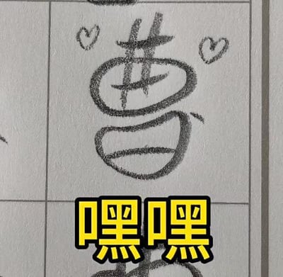 这是一张在方格练习本上的原创手写涂鸦图，将汉字“曹”用圆润的线条进行风格化书写，在字的左右上方还画了两个小巧的爱心图案，下方用黄底黑字的醒目样式标注了“嘿嘿”二字，整体风格搞怪可爱，是充满趣味的日常小创作，没有谐音梗或特殊暗示内容。