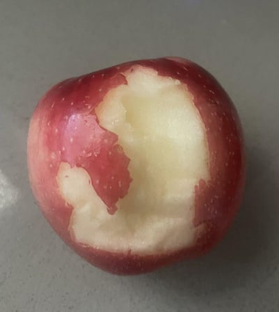这是一张真实拍摄的红苹果照片，苹果的部分红色果皮被去除，露出了质地细腻的米白色果肉，残留的果皮在果肉边缘形成了类似小熊轮廓的可爱形状，给普通的苹果增添了趣味感。