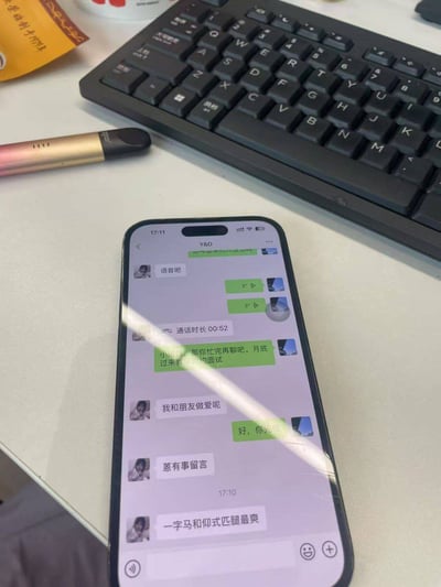 一张手机屏幕截图，显示了一段包含不当内容的聊天对话。手机放置在桌面上，背景中可见键盘、笔和其他物品。对话中出现了不适当的性暗示内容，如“我和朋友做爱呢”、“一字马和仰式匹腿最爽”等。
