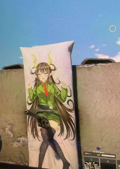 一张游戏截图被修改过的图片，展示了一个二次元风格的动漫抱枕被放置在坦克炮管之间。抱枕上印有一位穿着绿色军装、戴着红色领带、长着黄色牛角的少女，她有着长长的棕色头发和黑色过膝袜，表情娇羞，双手举起。坦克炮管的位置恰好从少女腿部前方伸出，形成一种滑稽的视觉效果。背景是游戏中的蓝天和云层，右下角可以看到游戏界面元素，包括距离指示器（0.27km）和弹药计数（1/47/6）。