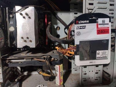 这张图片呈现了一台使用已久、内部积灰且线材略显杂乱的台式电脑机箱内部场景。机箱中已安装带有「GIGABYTE（技嘉）」标识的独立显卡，以及印有「VSP」字样的CPU散热器，各类供电线材缠绕其中。在机箱右侧，放置着一个未拆封的金士顿A400系列240GB固态硬盘，显然是用户准备为这台老电脑进行存储硬件升级，以此提升电脑的运行速度与存储性能。