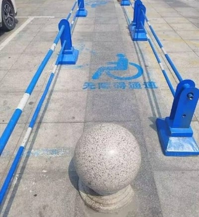 图片展示了一条标着“无障碍通道”的通道（地面有明显的轮椅标志和对应中文），但入口处却被一个水泥球体彻底挡住，造成实际无法通行。形成明显的讽刺与反差，让人哭笑不得。该配图常被用来吐槽实际工作中“形式主义”、“表面功夫”的现象。双关点在于“无障碍”与“有障碍”的现实对比，非常适合做社会问题相关二创或喷管理。

暗示：形式主义、官僚表象、设计不合理。
