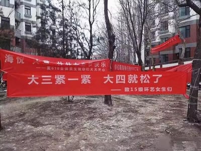 这是一张在国内某高校户外拍摄的实拍图，地面留有残雪，背景是校园宿舍楼和光秃的树木，前景悬挂着三条红色横幅。最下方的横幅最为醒目，内容为“大三紧一紧 大四就松了 —— 致15级环艺女生们”，这句话运用了双关梗，表面意思是劝导大三女生抓紧时间努力学习，到了大四就能轻松下来，实际带有低俗的性暗示；上方的两条横幅，一条写着“海悦  快乐 ——美618全体男生祝你们天天开心”，另一条部分文字被遮挡，可见“你们看到我们的XX了吗”的字样，整体是高校男生在类似女生节的校园节日中，为女生制作的趣味玩梗横幅。