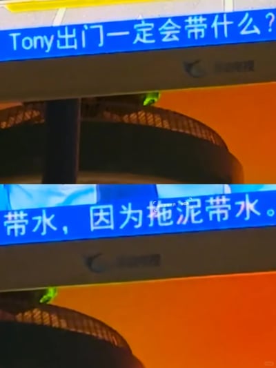 这是一张上下拼接的电视节目视频截图，画面以蓝色背景的白色字幕呈现趣味问答内容：上方字幕提出问题“Tony出门一定会带什么？”，下方字幕给出答案“带水，因为拖泥带水。”，该内容利用“Tony（托尼）”与“拖泥”的谐音关系制造笑点，属于谐音类冷幽默。图片中间偏右位置带有小红书用户“小虞看世界”的水印，表明该截图是从节目中截取后在小红书平台分享的内容。