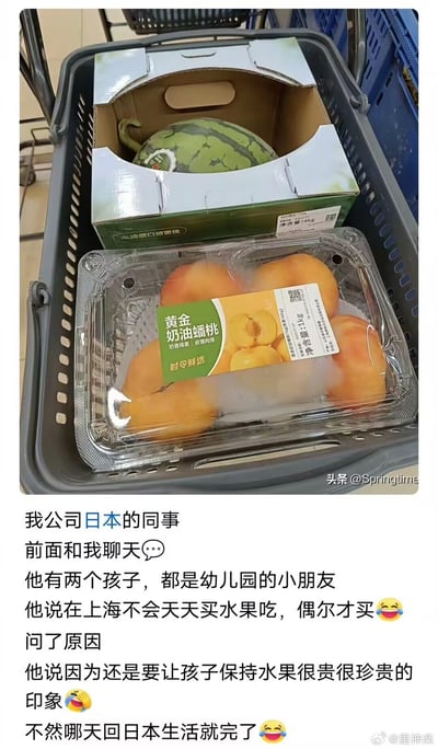 这是一则图文结合的社交媒体分享内容，上半部分是超市购物场景的实拍照片：灰色超市购物篮内放置了两盒生鲜，上方是一个开口的纸质礼盒，盒内装着一颗带皮的西瓜，下方是透明塑料盒装的黄金奶油蟠桃，盒身贴有产品标签和净含量标识。下半部分是配文，讲述作者的日本同事在上海生活时不会天天购买水果，仅偶尔购买，原因是要让自己两个正在上幼儿园的孩子保持“水果很昂贵珍贵”的印象，避免以后回到日本生活时无法适应日本更高的水果价格，配文附带了多个搞笑表情，内容轻松幽默。