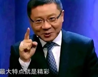 图片中一位穿着深色西装、内搭白色衬衫并系着蓝色花纹领带的中年男性，戴着眼镜，右手食指向上伸出，表情自信且略带微笑。背景为深蓝色幕布，整体给人正式且强调的感觉。图片底部有白色文字“最大特点就是精彩”，推测是在强调某事物的突出亮点。