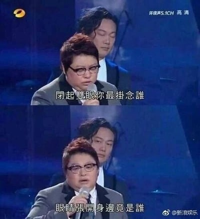 这是一张上下对比的视频截图拼接图，画面来自舞台表演场景，上方图中韩红手持话筒正在演唱，身后的陈奕迅闭着双眼，配文“闭起双眼你最挂念谁”；下方图中韩红依旧在演唱，身后的陈奕迅睁开了眼睛，配文“眼睛张开身边竟是谁”。这两句是陈奕迅歌曲《人来人往》中的歌词，结合画面里两人的位置和状态，形成了一种有趣的反差效果，仿佛歌词在描述陈奕迅的视角，制造出幽默的氛围。