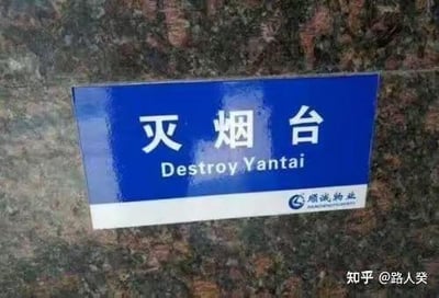 这是一张拍摄的物业设置的灭烟台标识牌照片，标识牌为蓝底白字的样式，上方是中文“灭烟台”，下方的英文翻译错误地将其处理为“Destroy Yantai”，把用来熄灭烟头的“灭烟台”，错误音译成了“摧毁烟台”，形成了搞笑的谐音翻译乌龙。
笑点解析：这里的乌龙是翻译时混淆了“灭烟台”（烟灰缸类的灭烟设施）里的“烟台”和城市“烟台”，使用了错误的英文表达，造成了极具反差感的歧义效果。