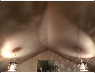 这张图片展示了一个室内天花板的视角，画面中有两盏悬挂的吊灯，灯光在天花板上形成了圆形的光晕。天花板和墙壁的交界处形成了明显的角落线条。图片整体呈现出旋转模糊的效果，给人一种动态的视觉感受。下方可以看到一面镜子，反射出房间的部分景象。