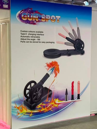 这是一张产品宣传海报，展示了一款名为"GUN SPOT"的产品。海报主体是一个黑色的玩具炮状装置，配有多个不同颜色（粉色、灰色、黑色、红色）的长条形配件，这些配件形状明显类似男性生殖器。海报上方有产品名称"GUN SPOT"，下方展示了产品使用时的效果，有火焰和爆炸的特效。产品特点包括：可定制颜色、Type-C充电接口、自动伸缩、180度角度调节以及配件可收纳便于包装。

图片存在明显的性暗示，通过将产品配件设计成生殖器形状来吸引眼球，属于利用低俗暗示进行营销的案例。
