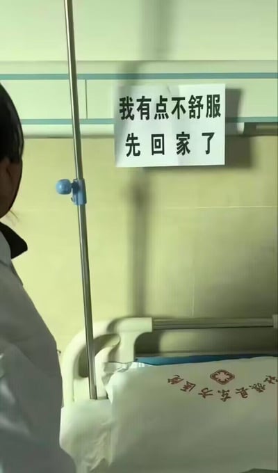 这是在社旗县东方医院病房内的实拍场景，病床上的被子印有「社旗县东方医院」的字样，墙面贴着一张纸条，上面写着「我有点不舒服 先回家了」，画面左侧能看到一位医护人员的背影。本该在病床接受治疗的病人，却以「不舒服」为由自行回家，形成强烈的反差感，制造出荒诞的黑色幽默效果，让人忍俊不禁。