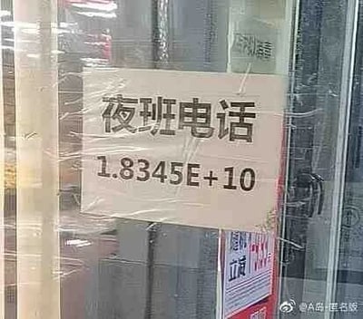 这是一张原始拍摄的静态图，画面展示了贴在玻璃门上的白色标识，标识上方用黑色字体写着“夜班电话”，下方本该显示的联系电话号码被系统自动转换为科学计数法格式“1.8345E+10”。这种情况通常出现在电子文档或表格中输入较长数字时，系统为了显示便捷将其转换为科学计数法，但被直接打印出来后，导致原本的电话号码无法被直接识别使用，形成了一个职场场景里的小乌龙，显得十分滑稽。标识被透明胶带固定在玻璃上，玻璃后方还能看到其他张贴物，图片右下角带有“@A岛匿名版”的水印。