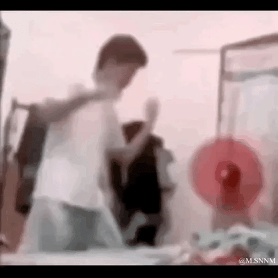 这是一段搞笑的动态GIF，画面中穿白色上衣的男子做出挥拳的动作，一旁穿黑色衣服的同伴立刻夸张地身体后仰，假装被打到，两人配合上演了一出无厘头的假打戏码，充满了搞怪趣味，让人忍俊不禁。