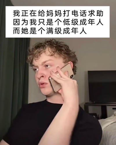 这是一张文字加注的静态真人图像，图中一位卷发的年轻男性眉头紧皱，表情苦恼焦虑，正手持手机贴在耳边打电话，看起来正处于窘迫的求助状态。图片上方配有文字“我正在给妈妈打电话求助 因为我只是个低级成年人 而她是个满级成年人”，借用游戏里“低级”“满级”的等级划分梗，调侃刚步入成年阶段的年轻人，在面对生活难题时缺乏经验和解决能力，依然依赖生活经验丰富、能应对各类问题的妈妈，精准戳中部分成年初期年轻人的生活状态，引发共鸣。