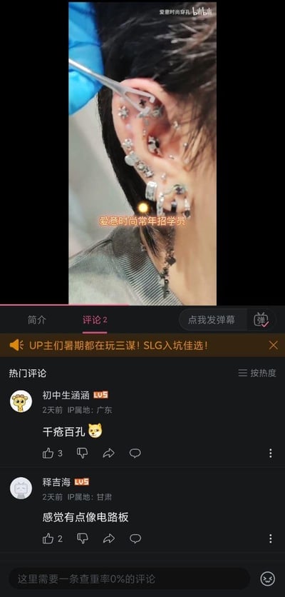 图片上半部分为视频截图，展示一只戴满各种金属饰品的耳朵，一名戴蓝色手套的人正用镊子调整耳饰，画面中央有橙色文字“爱慧时尚常年招学员”。下半部分是B站评论区界面，显示两条热门评论：“初中生涵涵”评论“千疮百孔”并配小黄脸表情，“释吉海”评论“感觉有点像电路板”，两条评论均带有IP属地（广东、甘肃）和发布时间（2天前）。