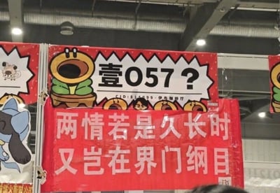 图片展示了一个在展会或活动中悬挂的红色横幅。上方横幅有一个卡通花盆形象，旁边写着"壹057?"和"CID:815-099-伊布咖啡厅"。下方红色横幅上写着改编自秦观《鹊桥仙》的诗句："两情若是久长时又岂在界门纲目"，将原句的"朝朝暮暮"改为生物学分类单位"界门纲目"，形成幽默效果。