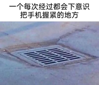这张图片展示了一个斜向铺设在地面的方形下水道井盖，井盖的格栅缝隙宽度看起来恰好可能让手机滑落。图片上方配有文字“一个每次经过都会下意识把手机握紧的地方”，精准捕捉到了人们日常手持手机行走时，看到这类井盖会产生的本能焦虑——担心手机不慎掉入缝隙，因此会下意识握紧手机，引发了大众对日常出行小细节的强烈共鸣。