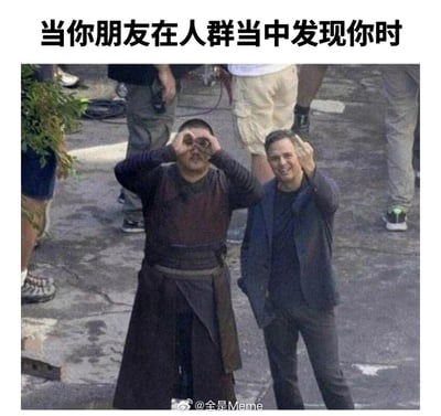 这是一张趣味梗图，上方配有文字“当你朋友在人群当中发现你时”，图中是漫威电影的片场路透画面，两位男士（其中一位是饰演漫威宇宙中绿巨人布鲁斯·班纳的演员马克·鲁法洛）分别用双手和单手做出望远镜的手势放在眼前，脸上带着兴奋、开心的神情，生动地还原了现实里朋友在人群中找到自己时，那种夸张又充满热情的打招呼状态，精准捕捉到了朋友间相处的趣味瞬间，让人感同身受。