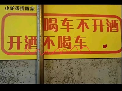 这是一张拍摄于线下的创意警示标语图，画面由两块黄色的提示牌组成，中间被一根金属立柱垂直隔开。左上角标注有“小炉香提醒您”的字样，原本的酒驾警示语“喝酒不开车，开车不喝酒”，因为立柱的分隔和两块牌子的排版，视觉上错位拼接成了“喝车不开酒，开酒不喝车”的趣味内容。该标语利用汉字谐音和视觉错位的创意手法，将严肃的酒驾警示用诙谐的方式呈现，既保留了原本的警示意义，又通过有趣的形式增强了传播性和记忆点，适合提醒餐饮门店用餐后驾车的顾客注意遵守交通规则，切勿酒后驾车。