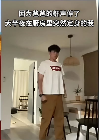 图片中一名男子深夜站在厨房内，身穿白色印有红色字母的T恤和棕色长裤，身体僵硬呈定住状态。上方文字说明“因为爸爸的鼾声停了 大半夜在厨房里突然定身的我”，生动展现了因家人异常安静而瞬间警觉的家庭日常场景，带有幽默又真实的生活气息。