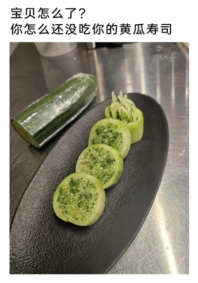 这是一张带有搞笑梗的美食内容图，上方配文“宝贝怎么了？你怎么还没吃你的黄瓜寿司”，图中展示的“黄瓜寿司”完全由黄瓜制作，没有常规寿司的米饭、馅料等元素：一段削去外皮的黄瓜被分成几部分，其中三段是将黄瓜内部搅碎后保留在瓜皮里的切片，外观类似寿司的截面，还有一段是被掏空后装入黄瓜丝的瓜圈，旁边还摆放着剩余的半段带皮黄瓜，用完全使用单一食材的方式，玩了“黄瓜寿司”的文字梗，制造出和大众认知中寿司的反差，形成搞笑的整活效果。