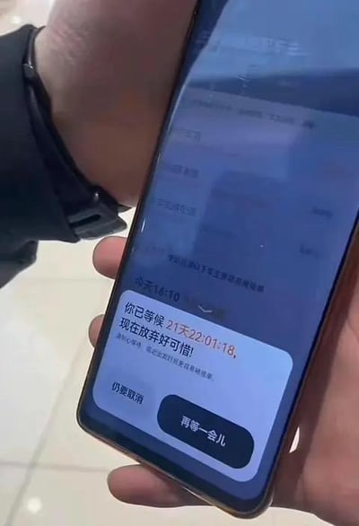 这是一张手机设备界面的截图，画面中一只手拿着手机，屏幕上弹出一个提示弹窗，显示当前时间为今天16:10，提示用户已经等候了21天22小时1分18秒，还配有文字“现在放弃好可惜！”，弹窗下方设有“仍要取消”和“再等一会儿”两个操作按钮。这个等待时长远超正常的服务等待或加载时间，属于夸张化的设计，用来调侃生活中那些让人感觉无比漫长的等待经历，带有搞笑和讽刺的效果。