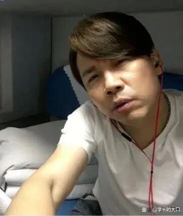 这是一张利用拍摄角度制造视觉错位效果的搞笑自拍照片，画面中的男子身着白色短袖，佩戴红色入耳式耳机进行自拍，其头部旁侧的床铺靠枕与自身脸部的轮廓、色彩恰好形成了视觉错觉，看起来仿佛男子的半张脸是艺人李荣浩的面部，这种巧合的视觉错位制造出荒诞又搞笑的效果，十分有梗。