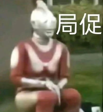 图片中是一位面部被模糊处理的人物，穿着红白色上衣，坐在户外环境中，背景有绿色植物。人物表情和姿态透露出一种不自然、尴尬的感觉，右侧配有醒目的白色文字“局促”，整体营造出一种尴尬、不自在的氛围。