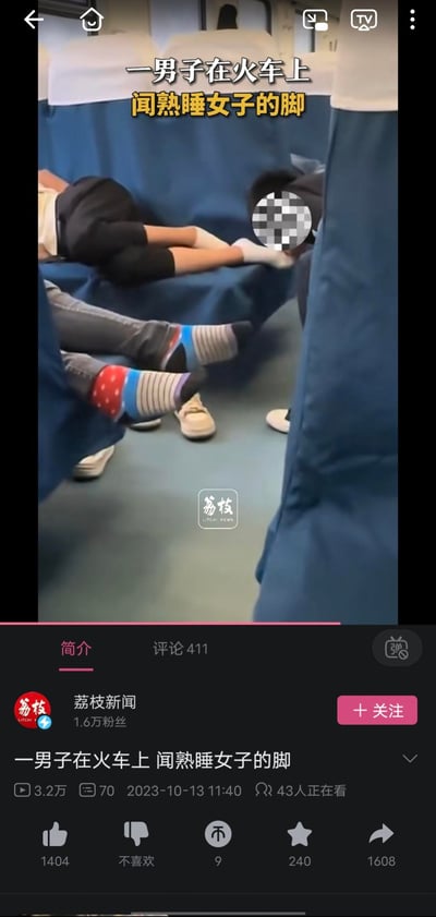 这是一张新闻视频截图，显示在火车车厢内，一名男子正靠近一名熟睡女子的脚部。女子穿着白色袜子，躺在蓝色座椅上。男子的面部被马赛克处理以保护隐私。周围可以看到其他乘客的腿部和鞋子。画面上方有黄色文字标题"一男子在火车上 闻熟睡女子的脚"。