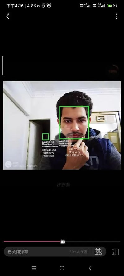 这是一张手机端直播的视频截图，画面主体是一位身处室内的男性，他的脸部被绿色识别框选中，旁边的墙面区域也被人脸识别系统错误识别为人物并框选。脸部的识别结果为：年龄25-28岁，性别男性（置信度0.97），情绪中性；墙面的识别结果为：年龄240-253岁，性别未知，情绪生气。画面底部是手机端的视频播放界面，显示“已关闭弹幕”，并有20+人正在观看，画面下方中间位置有“沙沙酱”的字样，左下角有模糊的平台标识。这张图展示了人脸识别系统出现的趣味识别错误，大概率是博主在直播中测试人脸识别技术的效果，呈现了系统的识别局限性。