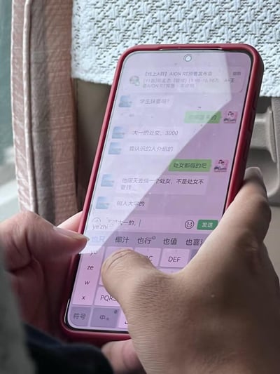 这是一张手持红色边框手机拍摄的微信聊天群截图，群名称为【线上A群】AION RT预售发布会，原本是汽车预售相关的群聊，却出现严重违反法律与公序良俗的非法性交易相关对话：一名群成员兜售声称是树人大学大一的“处女”，开价3000元，还提及“不是处女不要钱”的交易承诺，另一名群成员则质疑所谓“处女”的真实性，当前输入框正处于输入“大一的，”的状态。这类内容涉及卖淫嫖娼相关的非法交易，属于违法违规内容。