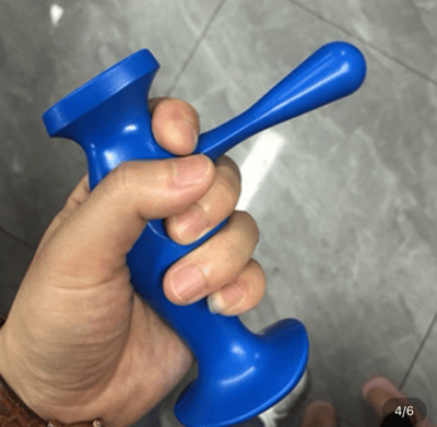 一只手握着一个蓝色的塑料工具，工具呈圆柱形，一端有一个类似杯口的开口，另一端有一个手柄。背景是灰色的瓷砖地面，右下角有"4/6"的标识，表明这可能是系列图片中的第四张。