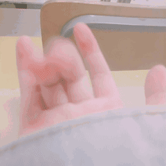 这是一段展示真人手部动作的动态GIF，画面中一只穿着浅色衣袖的手，手指做出类似比心的手势并快速晃动，手部呈现出模糊的动态效果，整体氛围轻松可爱，可用于向他人表达喜爱、亲昵的情绪，适合作为社交互动中的表情素材使用。