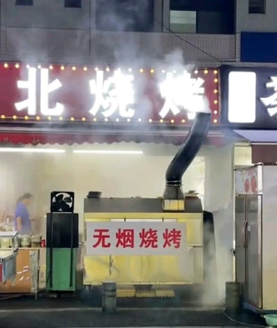 这张图片拍摄于一家烧烤店门口，烧烤摊机器上挂着大大的“无烟烧烤”标语，但实际上烟雾缭绕，非常搞笑，给人明显的反差感。所谓“无烟”实际上成了“全是烟”，属于现实与宣传不符的典型讽刺。适合用来吐槽各种名不副实、表面光鲜实际混乱的场景。

无明显双关语，但反差梗突出。