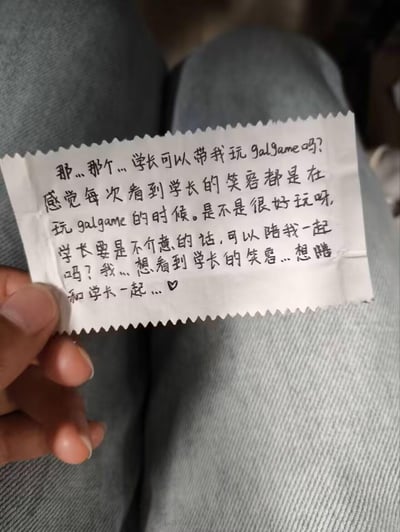 这是一张手持的边缘剪得参差不齐的手写小纸条，上面用腼腆的手写字体写着学妹的请求：想让学长带自己玩galgame，因为每次看到学长的笑容都是在玩这类游戏的时候，字里行间充满了青涩的心意，表达了想和学长一起、看到学长笑容的愿望，末尾还画了爱心符号，整体氛围充满校园青涩感。
没有双关、谐音梗或暗示内容。