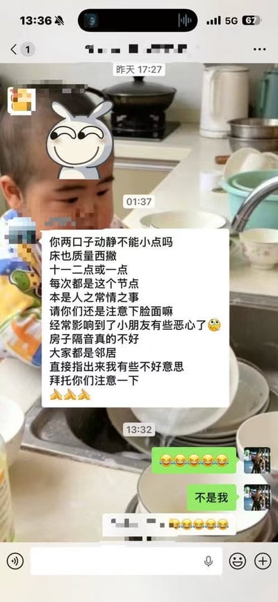 这是一张叠放于厨房实拍背景上的微信聊天记录截图，背景画面里的幼童额头处被贴了一个歪眼坏笑的卡通兔子贴纸。聊天内容为业主群内的邻居发消息投诉，称隔壁住户夫妻深夜十一二点到凌晨一点动静太大，加上房屋隔音差、床质量不好产生的噪音经常扰民，还影响到家中小朋友，希望对方注意影响。被提及的住户首先回复了一串笑哭表情，紧接着发送文字“不是我”撇清关系，随后还有其他群成员也发送了笑哭表情回应，整体场景充满尴尬又诙谐的搞笑效果。