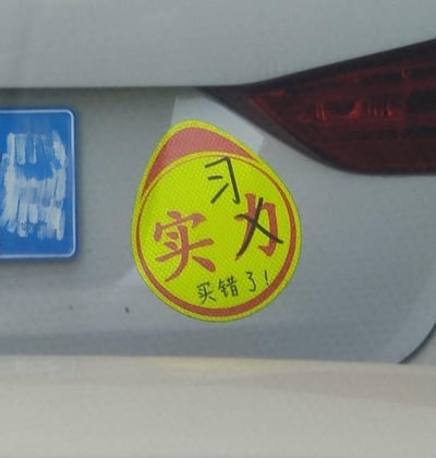 这是一张拍摄于汽车尾部的照片，展示了一张被手动修改的反光车贴：原本设计的「实力」字样被改成了「习力」，车贴下方还配有「买错了！」的文字。
这是通过修改车贴原有文字制造的趣味梗，利用改字的反差感，搭配「买错了」的吐槽，营造出搞笑接地气的效果，用来调侃自己买错车贴的小乌龙，充满趣味性。