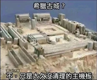 这是一张文字加注类静态搞笑梗图，利用视觉错觉效果，将一块长时间未清理、布满灰尘的电脑主板呈现出类似希腊古城遗迹的外观。图上方配有提问文字“希腊古城？”，下方给出反转回答“不，只是太久没清理的主机板”，通过这种视觉与文字的反差制造幽默效果，调侃电脑硬件长时间不清理后积灰严重的状态，左下角还有翻译标识水印“译：好色龙”。