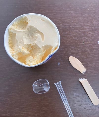 图中是一盒已经被挖过的冰淇淋，旁边有一个断成两半的塑料勺子和一把木质小勺。画面给人一种非常无奈又搞笑的气氛，暗示着用塑料勺挖冰淇淋时因为太硬导致勺子断了，最后只能换上木勺应急。这种日常小挫折非常有共鸣感，有“尴尬又无奈”的生活气息。

可以联想到“工具不给力”、“尴尬的生活小插曲”等主题。
本图没有双关语、谐音梗或明显的暗示，只是单纯地表现了现实窘境。