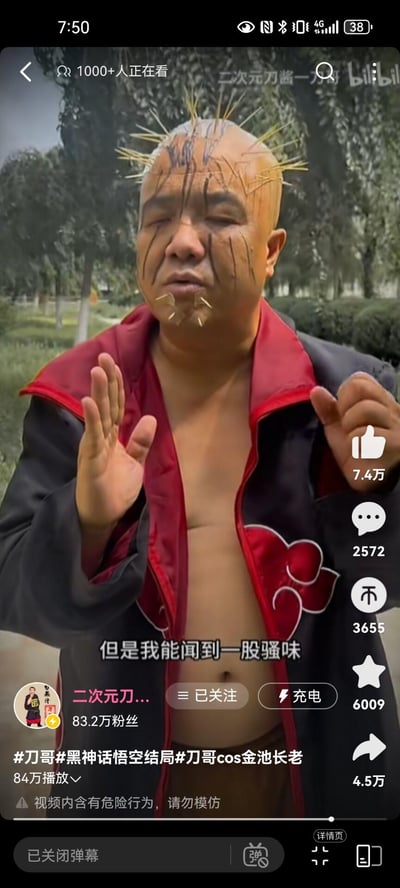 这是一张Bilibili视频截图，展示了一位名为"刀哥"的用户cosplay《黑神话：悟空》中的金池长老角色。图中人物穿着红黑相间的夹克，头发上插有尖刺状物体，面部画有类似胡须的黑色纹路。人物双手抬起，做出特定手势，背景是户外公园场景。视频界面显示有7.4万点赞，2572条评论，3655次分享，6009个收藏，以及84万次播放量。