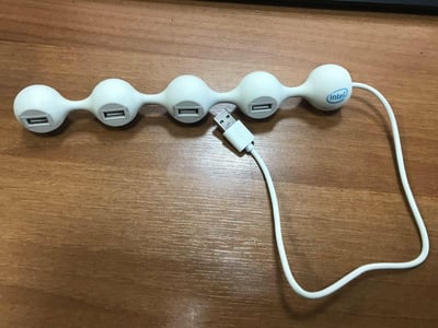一张展示Intel品牌USB集线器的照片。该集线器采用独特的球形设计，由五个相连的白色球体组成，每个球体侧面都有一个USB接口。集线器右侧连接着一根白色USB数据线，整体放置在木质桌面上。产品设计简洁现代，具有一定的视觉趣味性。