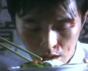 图片中是电影《功夫》中的经典场景，周星驰饰演的角色星仔面部带有血迹，正用筷子专注地从碗中吃面，眼神中透露出复杂的情绪，既有痛苦也有坚持，是影片中展现角色坚韧性格的重要画面。