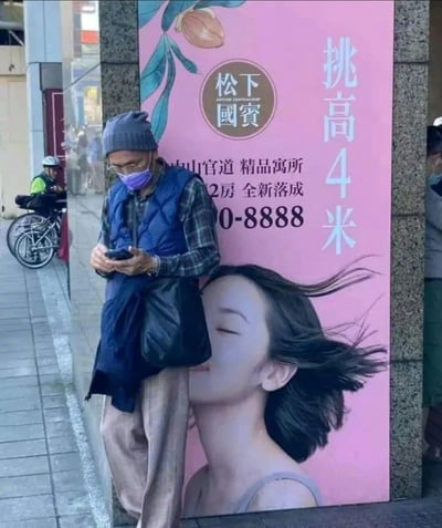 这是一张生活中偶遇的街头趣图，画面左侧是一位普通市民站在粉色广告海报前看手机。由于拍摄角度巧妙，站立者的身体正好与海报上的女性脖颈部位拼接在一起，让整张图出现一个非常夸张的漫画长脖子错觉，像是现实人物拥有了超长脖子，十分有趣和出其不意。图片整体营造出一种幽默、魔性并带点恶搞的氛围，是典型的错位摄影梗。没有发现谐音梗、暗示或双关含义，纯粹以视觉错觉制造笑点。