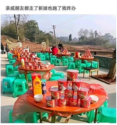 这是一张记录农村户外婚宴现场的静态图片，场地中摆放着多张铺有塑料桌布的圆桌，桌上没有传统婚宴的丰盛菜肴，取而代之的是统一摆放的桶装泡面、简易餐具和瓶装饮料，搭配的是常见的绿色塑料矮凳。原本应该坐满宾客的场地显得十分空荡，只剩零星几人在远处停留，背景是乡村的田野、树木和电线杆，充满乡土气息。图片上方配文“亲戚朋友都走了新娘也跑了我咋办”，营造出荒诞又心酸的氛围：这场婚礼显然突发变故，新娘跑路，宾客也随之散去，只留下准备好的简易“泡面席”，凸显出这场婚礼的闹剧性质和当事人的窘迫处境，用婚宴与泡面席的强烈反差制造搞笑效果。