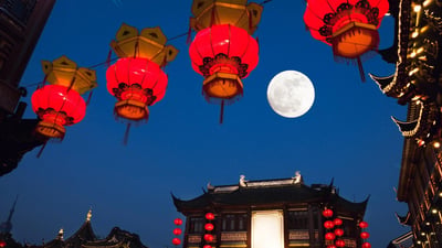 夜晚的中国传统街区，红灯笼与黄灯笼悬挂在空中，背景是一轮明亮的满月和传统中式建筑。红灯笼上有精致的黑色花纹装饰，灯笼下方有流苏垂下。建筑展现了典型的中国古典风格，飞檐翘角，灯火通明。整个画面营造出浓厚的节日氛围和传统文化韵味。