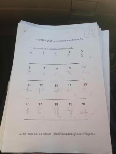 这是一张针对外国学习者的中文期末试题答题纸，右上角标注分数为22分。试卷包含两道题目：第一题要求将阿拉伯数字转换为中文大写数字，学生在书写1-10的中文大写数字（一到十）时全部正确，获得对勾；但从11开始，学生错误地将数字的中文写法进行笔画叠加创作，比如把“十一”的笔画堆叠在一起表示11，“十二”的笔画堆叠表示12，以此类推，11-19的答案被标注问号，20的错误写法被打了对勾。第二题是词语连线组词组的题目，尚未作答。试卷同时配有中文和泰文的题目说明，明确是面向泰国学习者的中文考试。