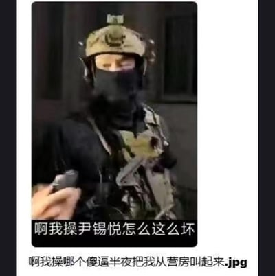 这张梗图展示了一名身着全套战术装备的特种兵，被人用手机近距离拍摄。图中配有两行吐槽文字：第一行是“啊我操尹锡悦怎么这么坏”，第二行是“啊我操哪个傻逼半夜把我从营房叫起来.jpg”。通过严肃的特种兵形象与接地气的烦躁吐槽形成强烈反差，表面看似在吐槽特定人物，实际核心是表达被半夜突然叫醒的极度烦躁与无奈，用这种反差感制造出搞笑的效果。