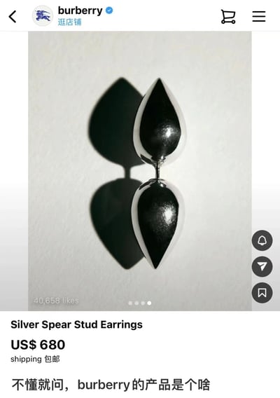 图片展示了Burberry官方店铺页面的一款银色耳钉产品，耳钉为水滴状银色金属材质，上下两个对称的锥形结构相连，背景为纯白色。页面显示产品名称为“Silver Spear Stud Earrings”，售价US$ 680并提供包邮服务，下方有40,658个点赞。图片底部添加了中文文字“不懂就问，burberry的产品是个啥”，表达了对该款耳钉设计或价值的困惑与调侃。