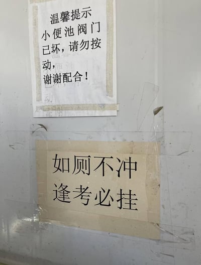 这是在卫生间墙面上张贴的两张提示标语：上方是一张白色纸张的温和提示，写着「温馨提示 小便池阀门已坏，请勿按动，谢谢配合！」；下方是一张泛黄纸张，用透明胶带固定，写着「如厕不冲 逢考必挂」。用学生群体在意的「逢考必挂」作为威慑，和上方的常规提示形成强烈反差，用搞笑接地气的方式督促大家保持卫生间卫生，很符合校园类场所的风格。