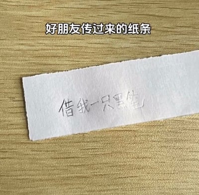 图片展示了一张被撕成条状的白色便签纸，放置在浅色木质桌面上。便签纸上用黑色手写体写着“借我一只黑笔”，上方有一行白色加粗文字标注“好朋友传过来的纸条”。整体场景呈现出日常生活中朋友间借东西的轻松互动，可能发生在校园或办公室环境中，充满了 casual 的温馨感。